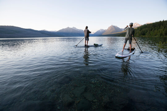 A man and woman stand up paddle boards (SUP) on Lake McDonald in Glacier National Park.
