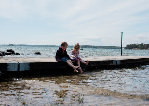 Brother and sister sitting on a jetty at the beach paddling their toes