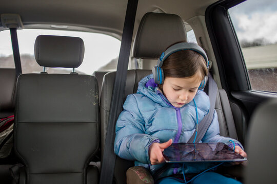 Front view of a small child in a carseat watching a tablet screen