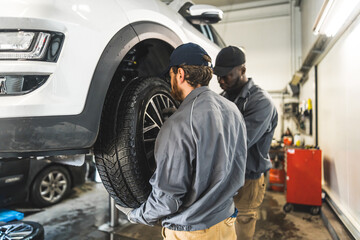 Car mechanics replacing wheels of a lifted automobile in a repair service station. High-quality photo