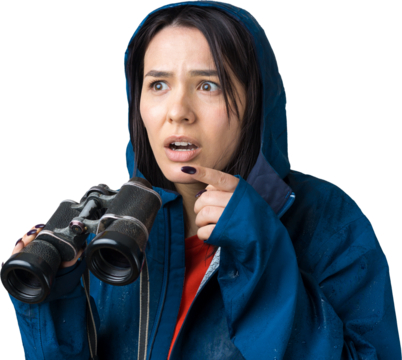 A tourist girl in a blue raincoat holds binoculars in her hands and looks into the distance, spies.