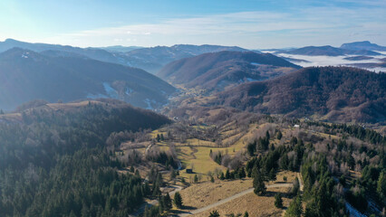 Fototapeta premium Aerial view of a small village in Carpathian Mountains of Romania. Thick mist covering a nearby valley