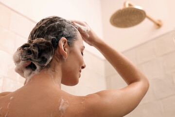 Naklejka premium Woman washing hair while taking shower at home, back view