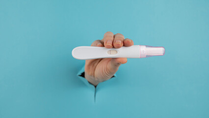A hand with a negative pregnancy test sticking out of a hole in a blue cardboard background. 