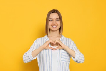 Young woman making heart with hands on yellow background. Volunteer concept