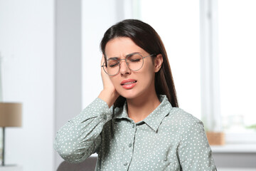 Young woman in eyeglasses suffering from ear pain indoors