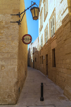 Narrow street in Mdina, Malta with sign showing the width and limestone walls