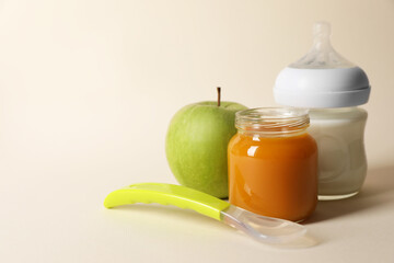 Healthy baby food in jar, bottle of milk, apple and spoon on beige background. Space for text
