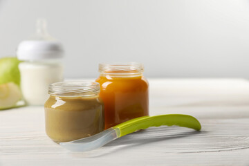 Jars with healthy baby food and spoon on white wooden table