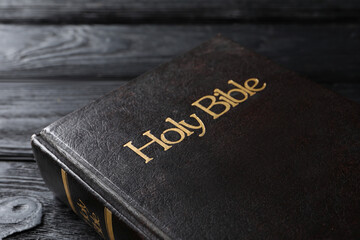 Bible with dark cover on black wooden table, closeup. Christian religious book
