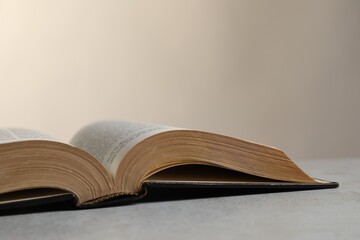 Open hardcover Bible on light grey table, closeup with space for text. Religious book
