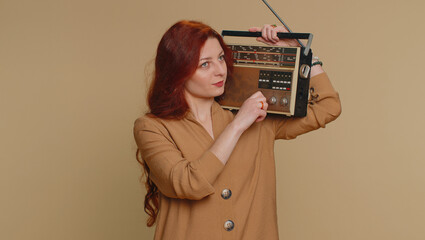 Redhead woman using retro tape record player to listen music, disco dancing of favorite track, having fun, entertaining, fan of vintage technologies. Young ginger girl isolated on beige background