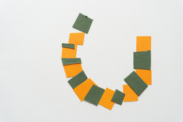 roundish shape composed of small square tiles in green and orange on blank paper