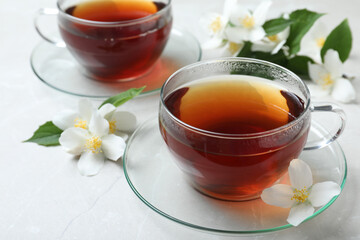 Cups of tea and fresh jasmine flowers on light grey marble table