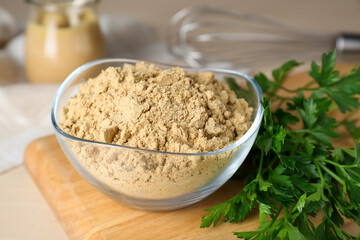Fototapeta na wymiar Bowl of aromatic mustard powder and parsley on wooden table, closeup