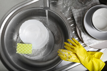 Washing plates, sponge and rubber gloves in kitchen sink, above view