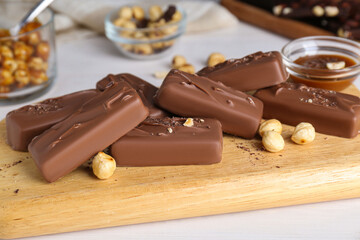 Delicious chocolate candy bars with nuts on white wooden table, closeup