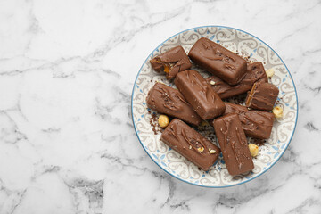 Delicious chocolate candy bars with nuts on white marble table, top view. Space for text