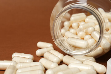 Open medicine bottle with pills on brown background, closeup