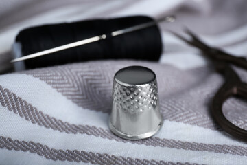 Silver thimble on striped cloth, closeup. Sewing accessory - obrazy, fototapety, plakaty