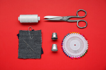 Flat lay composition with thimbles and different sewing tools on red background