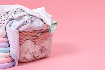 Laundry basket with baby clothes near toy on light pink background, closeup. Space for text