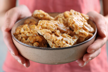 Woman holding bowl with delicious peanut kozinaki bars, closeup