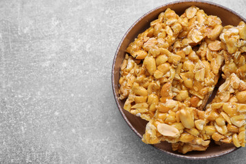 Bowl with delicious peanut kozinaki bars on light gray textured table, top view. Space for text
