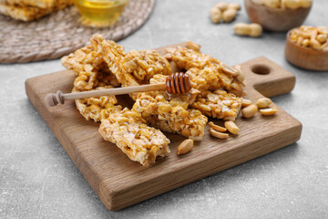 Delicious peanut kozinaki bars and honey dipper on light gray textured table