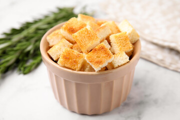 Delicious crispy croutons in bowl on white marble table, closeup