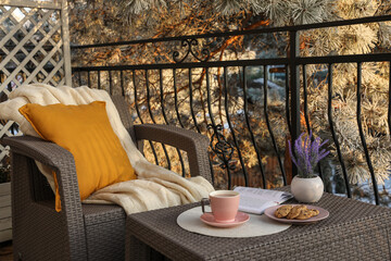 Cup with tasty cocoa, cookies and book on rattan table at balcony