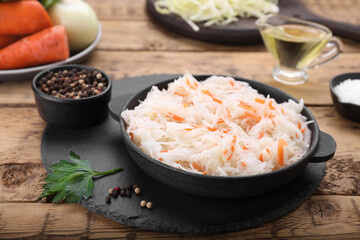 Bowl of tasty sauerkraut and ingredients on wooden table