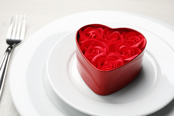 Decorative heart shaped box with roses on white dishware for romantic dinner on white table, closeup