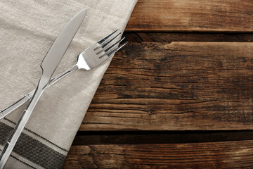 Fork, knife and napkin on wooden table, top view with space for text. Stylish shiny cutlery set