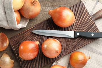 Many ripe onions and knife on wooden table, flat lay