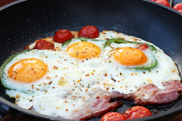 Delicious fried eggs with bacon, tomatoes and pepper in frying pan, closeup