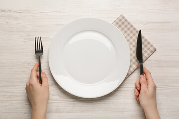Woman with empty plate and cutlery at white wooden table, top view
