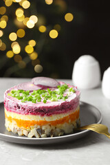 Herring under fur coat salad served on light grey table against blurred festive lights, space for text. Traditional Russian dish