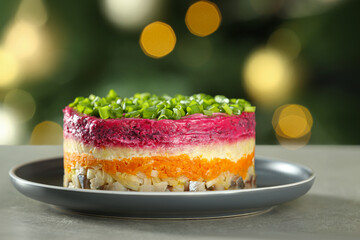 Herring under fur coat salad on grey table against blurred festive lights, closeup with space for text. Traditional Russian dish