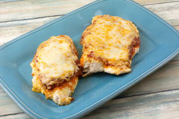 Chicken parmesan on serving plate with two chicken breasts and spicy marinara sauce