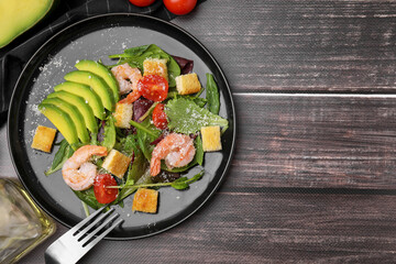 Delicious salad with croutons, avocado and shrimp served on wooden table, flat lay. Space for text