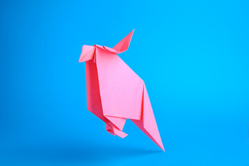 Origami art. Handmade pink paper parrot on light blue background