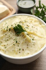 Bowl of delicious mashed potato with parsley on wooden table, closeup