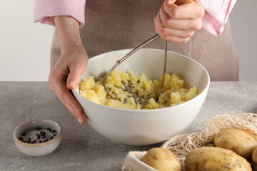 Woman making mashed potato at light grey table, closeup