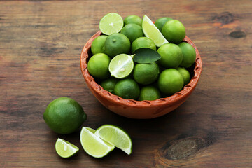 Whole and cut fresh ripe limes in bowl on wooden table