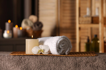 Spa composition with candle, orchid flower and rolled towel on massage table in wellness center,...