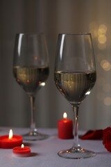 Glasses of white wine and burning candles on grey table against blurred lights. Romantic atmosphere