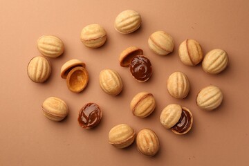 Homemade walnut shaped cookies with boiled condensed milk on pale brown background, flat lay