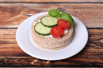 Tasty crispbreads, cucumber, tomatoes, cream cheese and basil on wooden table, closeup