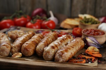 Tasty grilled sausages with vegetables on wooden board, closeup